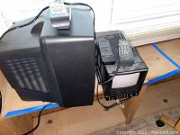 Side view of two CRT televisions and several remote controls on top, showing bulky design and connectors.