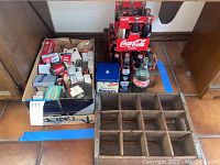 Photo of the lot including wooden crate with small vintage tins and boxes, Coca-Cola bottles in carriers and crate, and blue Krispy tin.