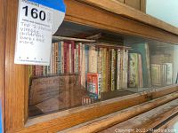 Top shelf of wooden bookshelf with glass door containing a row of children's books of various colors and sizes, including a small 'Snap' playing card game box and a postcard envelope.