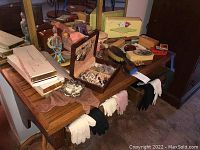 Wide view of wooden table displaying multiple vintage gloves, costume jewelry in a wooden case, perfume bottles, brushes, and assorted vintage boxes and tins.