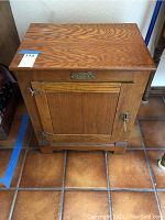 Front view of a vintage wooden ice box showing the wood grain and door with metal latch and hinges.