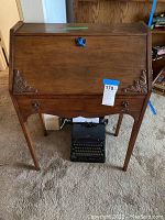 Full view of wooden secretary desk closed, showing decorative corner carvings and legs