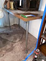 View of one corner of the rectangular vintage table showing wooden surface and one round metal tapered leg with adjustable foot