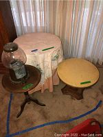 Three vintage tables arranged together, one covered with a cloth, shown in a room corner with carpeted floor and curtains.