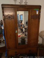 Front view of the vintage wooden wardrobe showing three doors and a central mirror, with a key hanging on the handle.