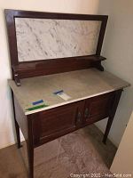 Side view of the vintage wash bowl table showing white marble top, marble backsplash framed with wood, and two front wooden cabinet doors with metal handles.