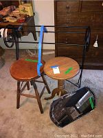 Photo showing a black metal blanket stand, two wooden stools, and a vintage beveled mirror leaning against the metal stand on carpeted floor.