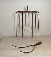 Photo of two rusty antique pitchfork heads metal working ends only on a wooden surface, showing front view of both items.