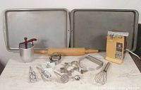 Baking sheets, rolling pin, various cookie cutters, hand beaters, whisk, dough blender, thermometer, piping tip, corer, and vintage electric can opener all displayed on a table.