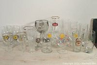Full lot of 16 collectible beer glasses arranged in two rows, showing various styles and logos including Chimay, Guinness, Stella Artois.