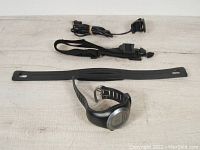 Garmin GPS watch with digital display, chest strap, extra watch strap, and charging cable on a white surface