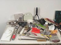 Overview of assorted kitchenware including brie baker, mandolin slicer, steamer, ladle, and utensils.