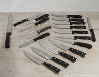 Top view of all knives arranged on light wood surface showing variety of sizes and handle styles