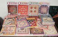 A spread of about 15 Quilter's Newsletter Magazine issues arranged flat, showing vibrant quilt patterns on the covers.
