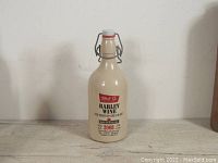 Full view of the ceramic swing top beer bottle, cream color with printed label showing brand and product details.