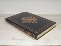 Photo of closed large hardcover atlas with ornate gold embossing on dark cover and spine.