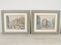 Two framed urban scene paintings shown side by side from the front