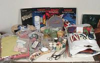 Wide view showing assorted sewing supplies including fabric bolts, multiple spools of thread, knitting needles, scissors, and Singer sewing books arranged on a flat surface.