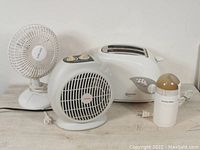 Photo showing white desk fan, white fan heater with two yellow dials, white two-slice toaster, and white coffee grinder with beige lid.