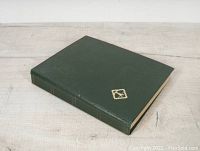 Closed green hardcover stamp album with a small gold emblem on the front cover.