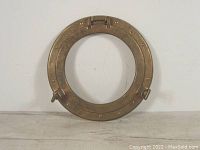 Front view of vintage brass porthole cover, showing round shape and fastening details