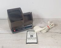 Photo of the GAF Pana Vue automatic slide viewer, power cord, and user manual arranged on a light wooden surface.