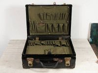 Open tool case showing green canvas lining with numerous tool pockets and compartments inside the lid and main body. Heavy duty black leather construction with brass hardware.