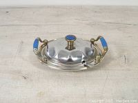 Top view of vintage stainless steel serving dish with lid closed showing blue inlay handles and lid knob, gold accents on the rim, handles, and knob.