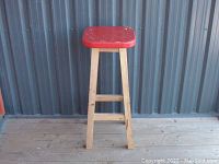 Front and side view of the vintage wooden workbench stool showing the red square seat, natural wood legs, and wooden floor setting.