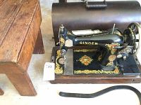 Close-up of antique Singer sewing machine with detailed gold and red decals, showing the front and top portion including the needle area and brand name.