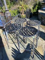 Photo of four metal bar chairs grouped together outdoors showing lattice seats and curved backs.