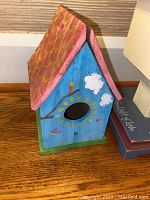 Colorful handmade wooden birdhouse with a sun and clouds motif and red shingled roof.