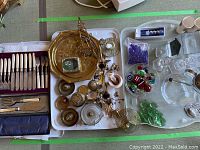Wide view of the collection showing brass items, flatware, glass pieces, and barware accessories all arranged on trays.