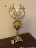 Full view of the lamp showing globe shade, brass reservoir, column, and base