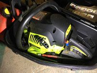 Poulan gas chain saw with visible green and black body and yellow primer bulb on fuel tank, inside black carrying case.