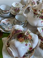 Photo of several china teacups and teapots with floral designs and gold trim, highlighting multiple pieces arranged close together.