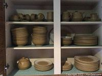 White cabinet shelf showing top row of stacked mugs and small pitchers