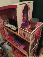 Dollhouse showing multiple levels with tea set on a shelf, furniture inside the rooms, and outdoor patio with a crank and seating.