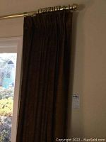 Photo capturing the velvet brown drapery panel hanging on a gold-toned curtain rod showing length and overall condition visible near window wall.