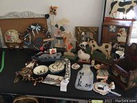 Full view of farm animal and country decor laid on black table including wooden figurines, ceramic milk jug, decorative wreath, and wall plaques.
