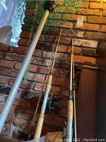Photo showing two fishing rods with attached reels leaning against a brick wall next to a metal framed fishing net with green netting.