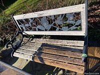 Full view of weathered wooden seat planks and metal frame with decorative floral backrest.
