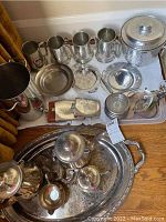 Wide shot showing silver-plated tea service on ornate tray, metal flasks, small hammered metal plates, Birks steins and large hammered ice bucket.