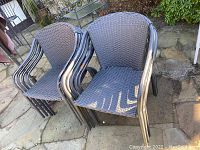 Nine black metal framed patio chairs stacked outdoors, showing woven seat and backrest material