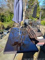 Full view of rectangular glass top table with umbrella and stacked chairs alongside other outdoor furnishings