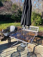 Full view of glass top patio table with umbrella and five stacked patio chairs nearby.