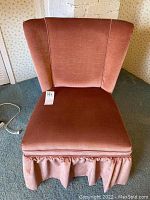 Front view of pink velvet slipper chair showing wingback and pleated skirt base.