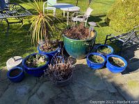 Overview of seven planters on patio showing green and blue glazed planters, some with soil and plants, and an empty small blue pot