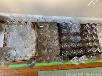 Overhead photo showing multiple trays filled with various clear glass and crystal stemware and cocktail glasses.