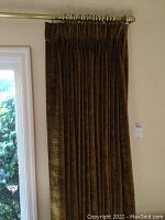 Brown velvet curtain panel hung on metallic rod in living room space, shows partial window and greenery outside.